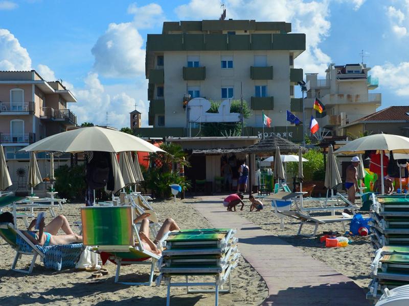 Spiaggia con lettini, ombrelloni e un edificio sullo sfondo sotto un cielo nuvoloso.