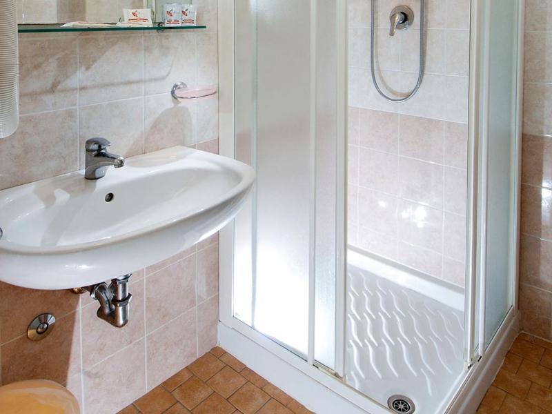 Bagno con cabina doccia, lavandino e piastrelle beige.